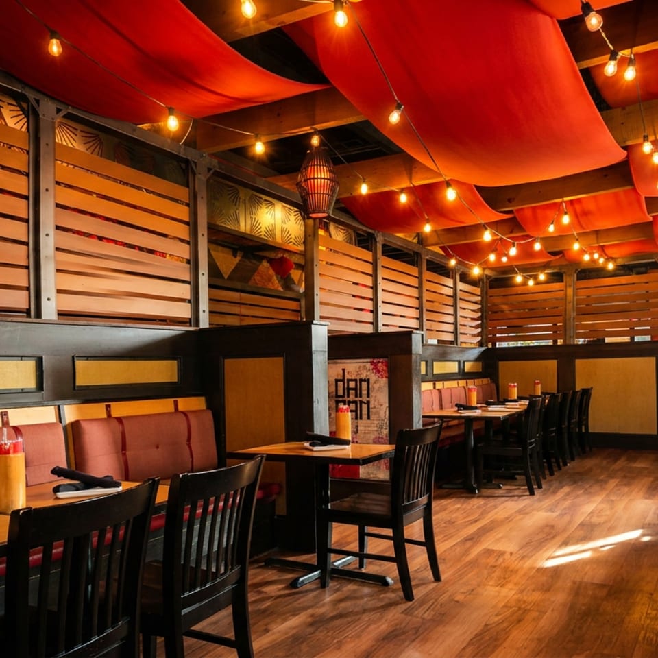 Restaurant interior with red fabric ceiling, string lights, wooden walls, and empty tables with chairs.