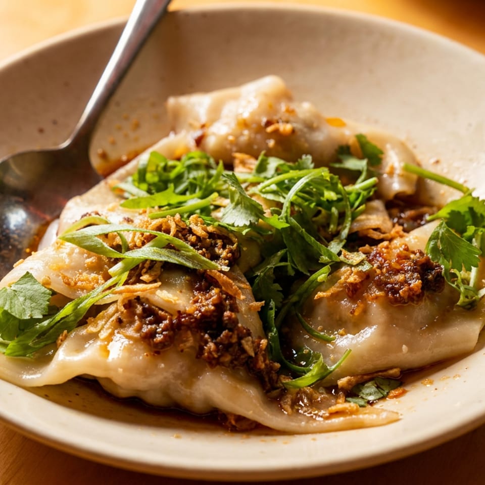 Plate of dumplings topped with cilantro, green onions, and crispy fried garlic, with a spoon.