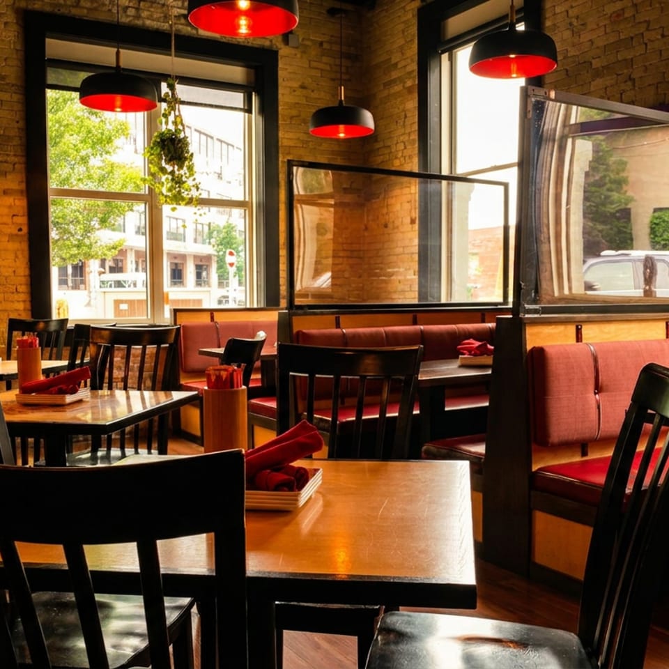Empty restaurant dining room with brick walls, red booths, dark tables, and red pendant lights.