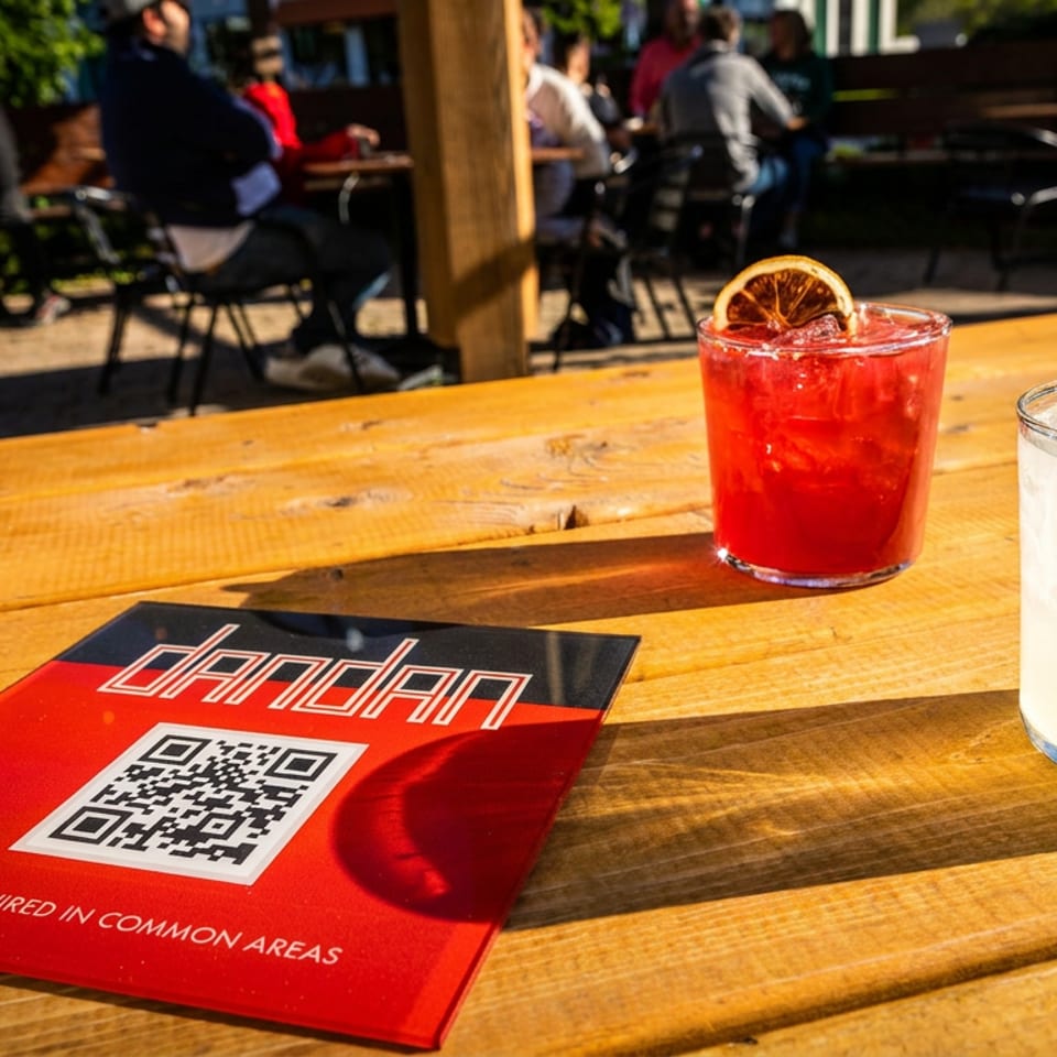 Two cocktails and a red Dandandan menu with a QR code on a wooden outdoor table.